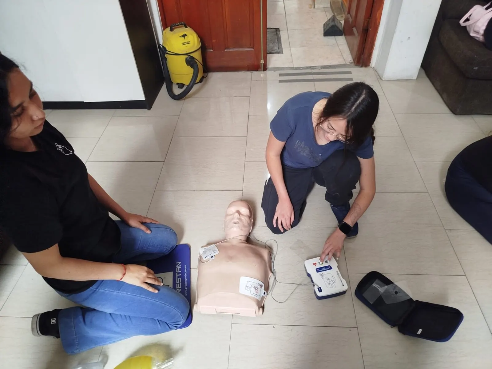 Dos alumnas practicando RCP en el suelo con un fantoma y un DEA