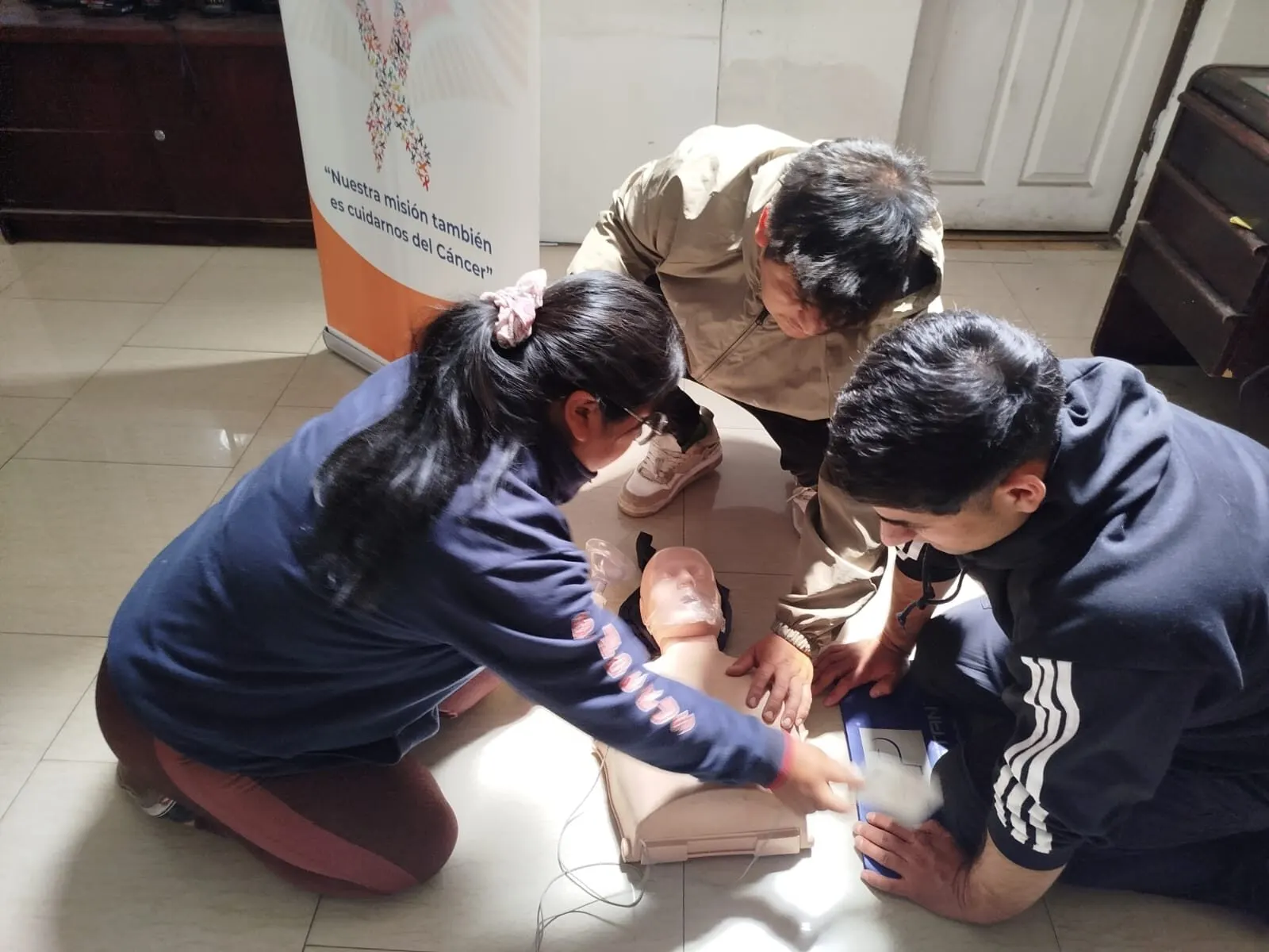 Dos alumnos practicando RCP sobre un fantoma junto a una instructora