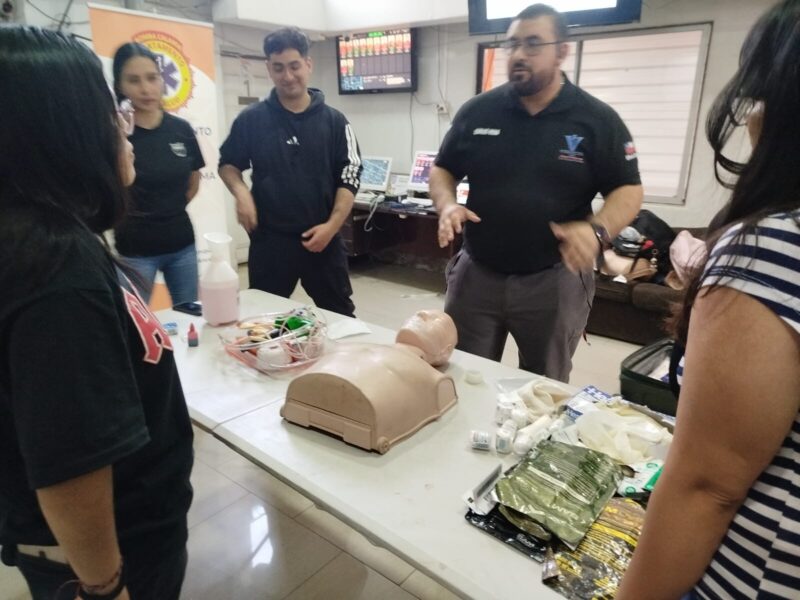 Instructor explicando junto a una mesa con simuladores de herida y botiquines
