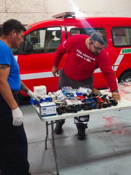 Instructor preparando insumos de trauma en una mesa junto a un carro de bomberos