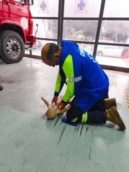 Bombero practicando ventilación en un fantoma de lactante, junto a un carro de bomberos