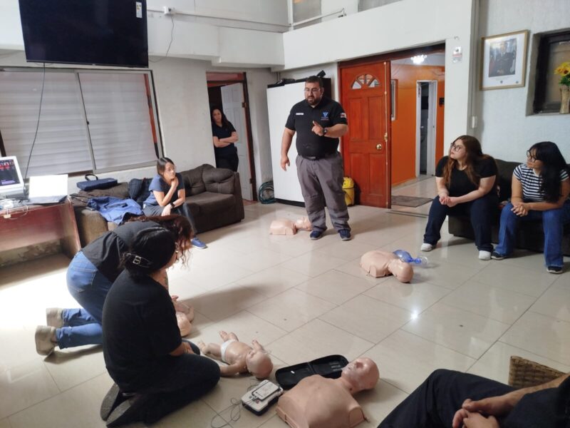Alumnos practicando RCP con fantomas en el suelo de una sala, con un instructor observando