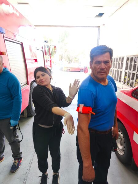 Alumna mostrando un torniquete puesto en el brazo de un compañero, junto a un carro de bomberos