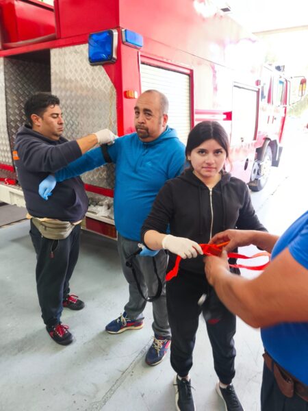 Alumnos practicando la colocación de un torniquete en el brazo, junto a un carro de bomberos